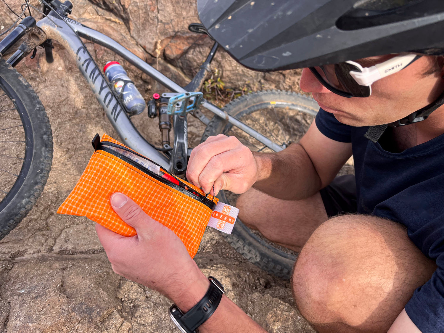 A mountain biker unzips a peak first aid kit to look inside at the contents