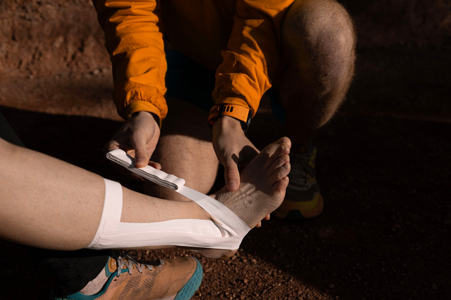 A person in a peak first aid jacket applies search and rescue approved first aid kit medical tape to an injured ankle