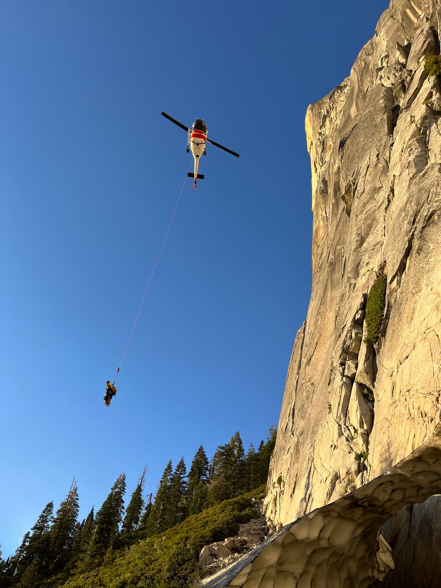 A helicopter next to a large cliff picks up an injured person